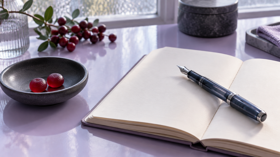 Illustrative blank notebook and pen beside two red gummies in a charcoal bowl on a lilac desk.