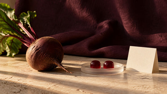 Illustrative beet and two ruby-red gummies beside a blank label card on a stone tabletop.