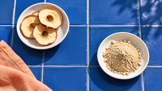 Illustrative dried apple rings and generic plant powder in separate white bowls on blue tiles.