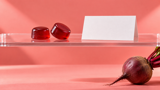 Illustrative red gummies and a blank label card on an acrylic shelf above a beet against a coral backdrop.